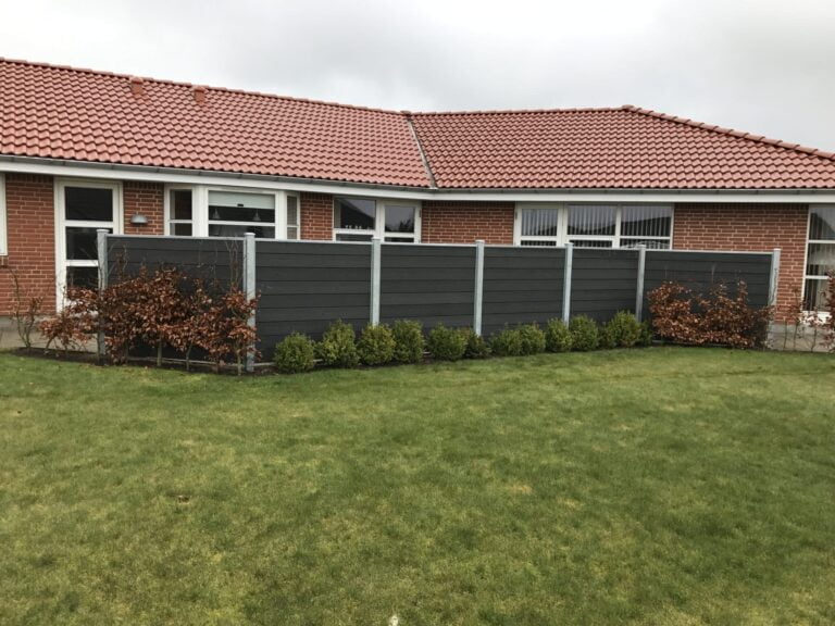 Rød murstenshus med græsplæne og hegn