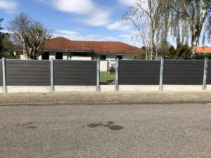 Gråt hegn foran hus med rødt tag.