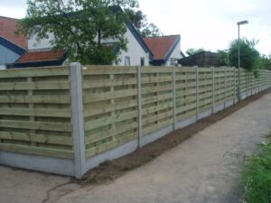 Træhegn ved sidevej nær hus med rødt tag.