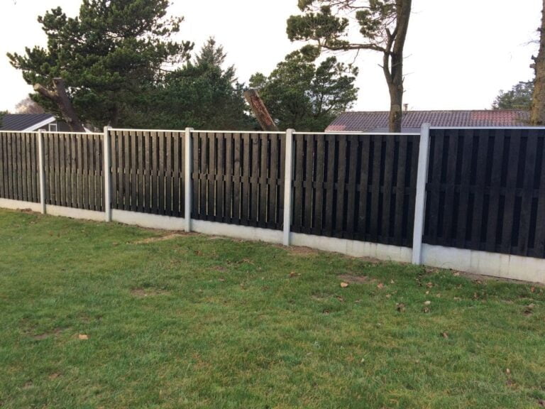 Sort hegn langs grøn græsplæne og træer.